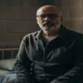 صورة تعبيرية تجسد إعلامياً بملامح وقورة وشعر رمادي يجلس بملابس بسيطة داخل غرفة توحي بأجواء القيد، مع خلفية لجدار حجري ونافذة صغيرة، تعبيراً عن الحالة الإنسانية لبرهان بسيس خلف القضبان.