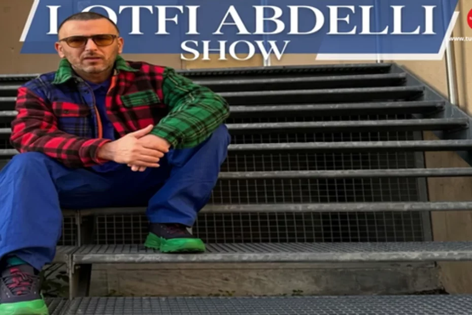 Image of Tunisian comedian Lotfi Abdelli wearing a bold Urban Style outfit, including a multicolor plaid jacket and royal blue trousers, with the text "LOTFI ABDELLI SHOW" at the top. This featured image relates to the latest news about his legal case and his unique fashion choices.