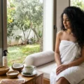 Comment Maintenir une Chevelure Saine, Forte et Éclatante ? Une image en gros plan dans un spa de beauté en Tunisie, montrant une esthéticienne en train de tamponner doucement les cheveux d'une femme avec un tissu doux, avec des ingrédients naturels comme le fenugrec, les pommes de terre et l'huile de Vitamine E présentés sur une table en bois, illustrant des techniques de soins capillaires.